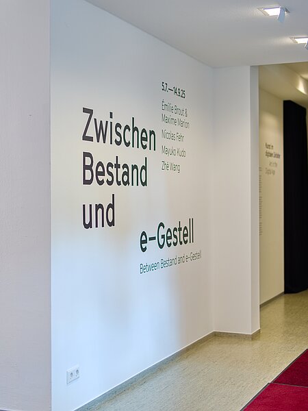 Wandinstallation mit Schriftzug: "Zwischen Bestand und e-Gestell" in großer, klarer Schrift. Darunter sind die Namen der Künstler Emilie Brout, Maxime Marion, Nicolas Fehr, Mayuko Kudo und Zhé Wang aufgelistet. Die Ausstellung läuft vom 5. Juli bis 14. September 2025.