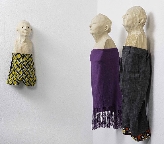 Drei Kopf-Skulpturen, welche unter ihrem Hals Hosen tragen.