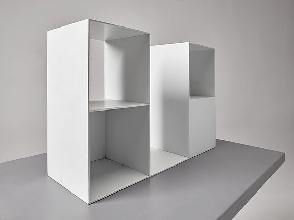 Das Bild zeigt eine Skulptur von Sol Lewitt. Es besteht aus einer Sockelplatte, auf der eine Form aus Stahlblech steht, die in Würfelform komponiert wurde und offene und geschlossene Flächen beinhaltet.