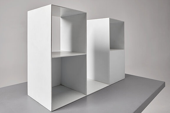 Das Bild zeigt eine Skulptur von Sol Lewitt. Es besteht aus einer Sockelplatte, auf der eine Form aus Stahlblech steht, die in Würfelform komponiert wurde und offene und geschlossene Flächen beinhaltet.